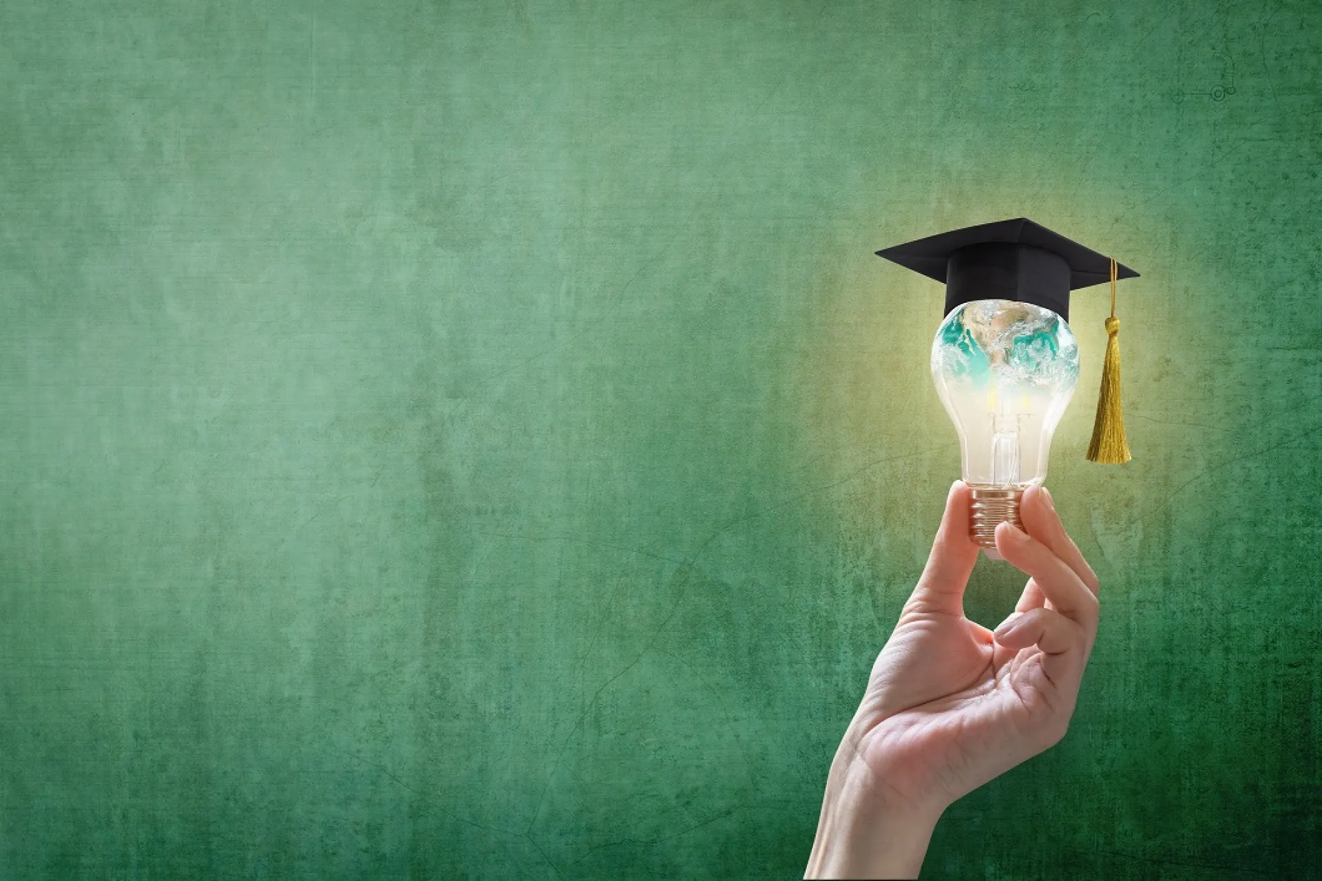 Hand houdt een gloeilamp met afstudeerhoed vast tegen groene achtergrond.