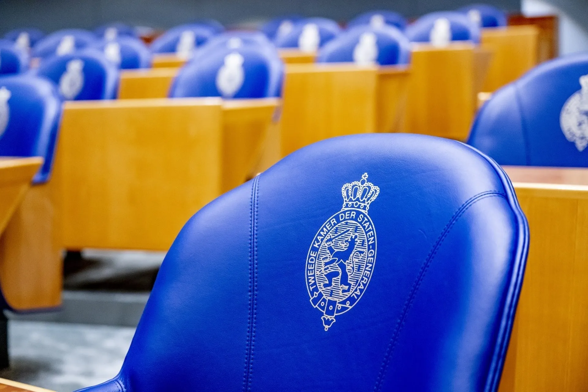 Blauwe stoelen met logo in de vergaderzaal van de Tweede Kamer