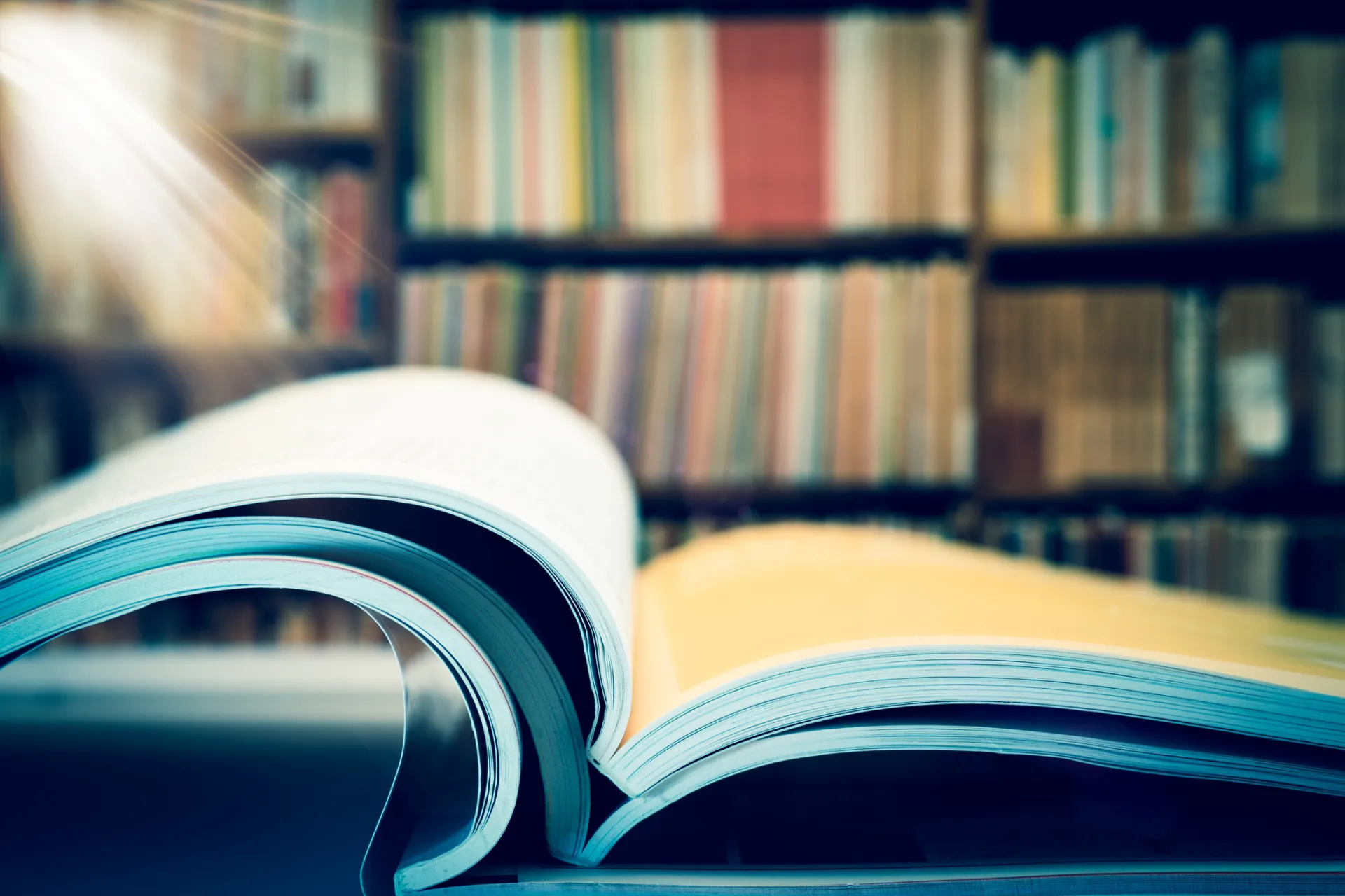 Een open boek in een bibliotheek met vaag op de achtergrond boeken op planken
