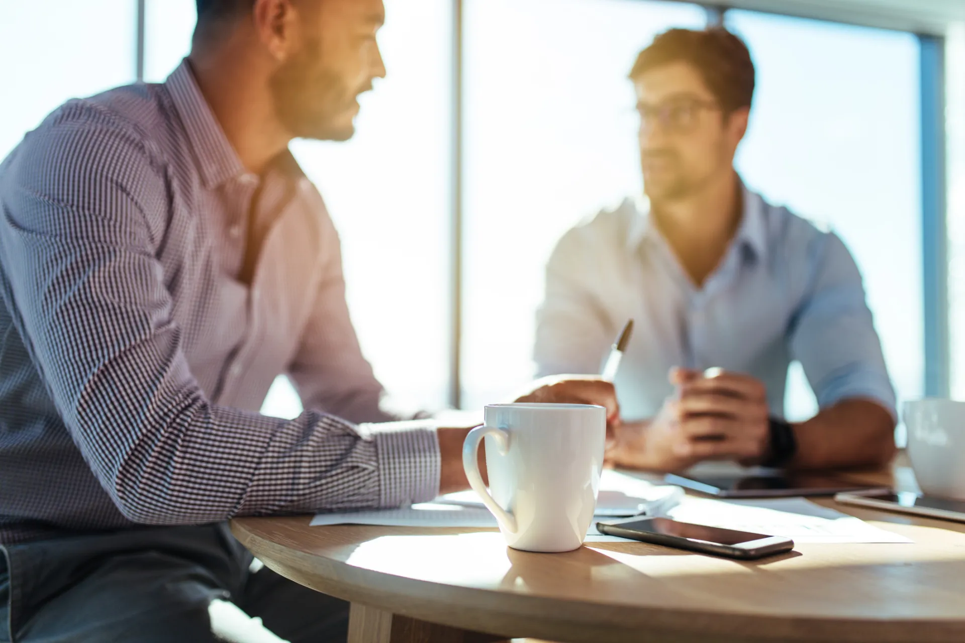 Twee mannen in gesprek tijdens een werkvergadering met koffiekopjes op tafel.